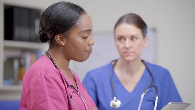 Two nurses with stethoscopes at nurses station review patient chart, rack focus