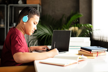 The young teenager wearing headphone for listening music,writing paper work,using laptop for searching data,blurry light around