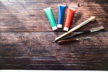 Obraz premium Red, green and blue paint tubes with paintbrushes in the wooden background