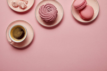 Top view of pink meringues, macaroons and cup of coffee on pink saucers with white dots on pink...