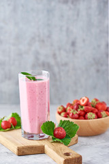 Strawberry smoothie in glass jar and fresh strawberries in wooden bowl on a cutting board