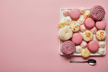 Flat lay with assorted meringues and macaroons on square dish with spoon on pink background