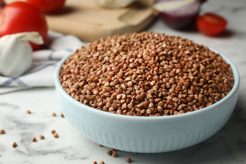 Bowl of uncooked buckwheat on marble table, closeup. Space for text