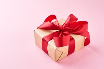 close up gift box in craft paper with red ribbon on a pink background