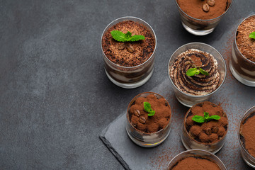 Group of portions of Classic tiramisu dessert in a glass cup on stone board on concrete background