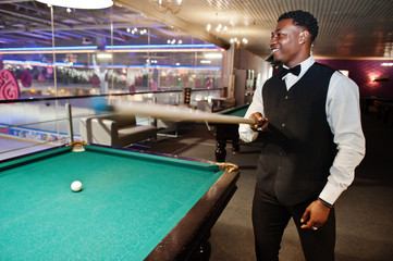 Young handsome african man wearing white shirt, black vest and bow tie play pool billiard.