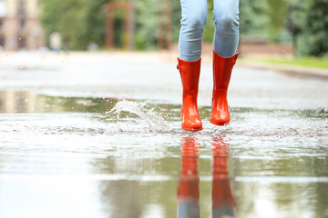 Woman with red rubber boots jumping in puddle, closeup. Rainy weather