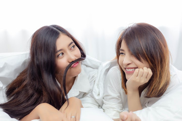 Obraz na płótnie Canvas Charming beautiful woman is laughing her cute friend for making joke. Attractive beautiful woman is making funny face by using hair put on mouth likes a mustache. They’re close friend, love each other