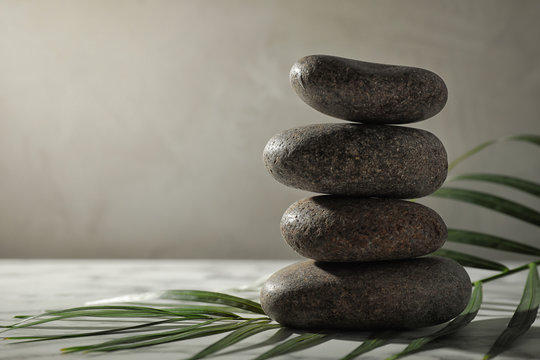 Stack of spa stones and palm leaf on grey table, space for text