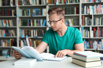 Young man reading book at table in library
