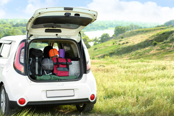 Car with camping equipment in trunk on green field. Space for text - obrazy, fototapety, plakaty