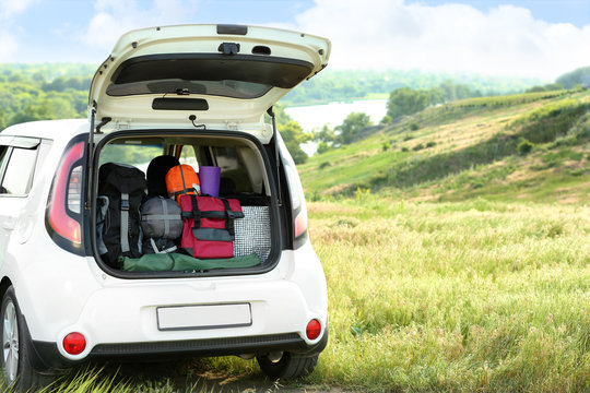 Car With Camping Equipment In Trunk On Green Field. Space For Text