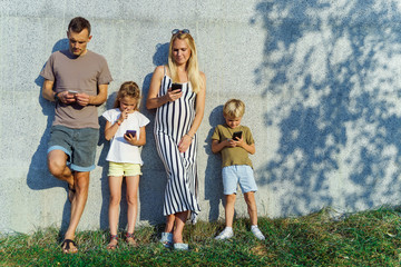 Image of parents and children with phones in their hands standing on concrete wall on street
