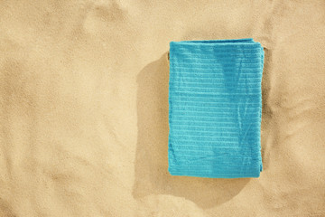 Folded new towel on sand, top view with space for text. Beach object
