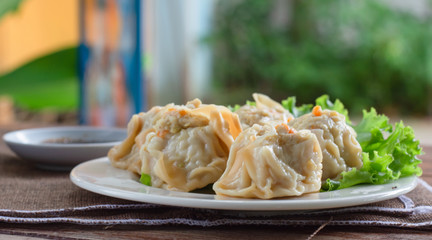 Chinese Steamed Dumpling (Shumai) on white dish served with soy sauce and .lettuce leaves on brown cloth and wooden table. Delicious Dimsum pork.