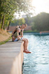 Image of young father and boy sitting on wooden bank by river