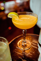 Glass of orange cocktail decorated with lemon at bar counter background.