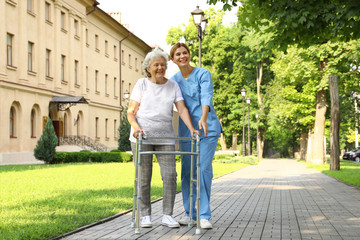 Fototapeta na wymiar Happy nurse assisting elderly woman with walking frame at park
