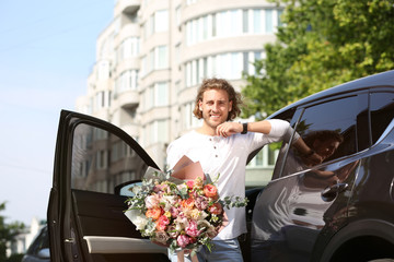 Young handsome man with beautiful flower bouquet near car on street