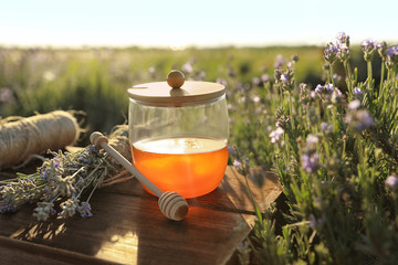 Jar of honey on wooden table in lavender field