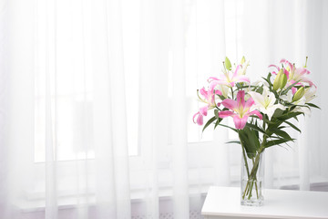 Vase with bouquet of beautiful lilies on white table indoors. Space for text