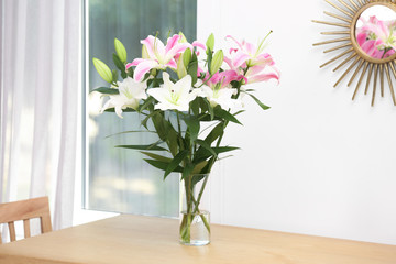 Vase with bouquet of beautiful lilies on wooden table indoors