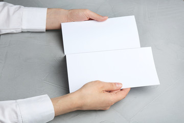Young woman holding blank brochure at grey table, closeup. Mock up for design