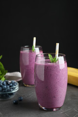 Glasses of delicious blueberry smoothie on grey table against black background