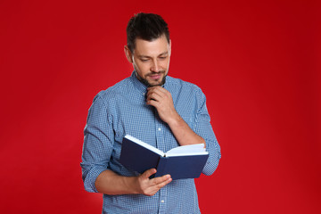Handsome man reading book on red background