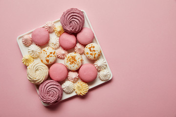 Fototapeta na wymiar Top view of assorted french macaroons and meringues on square dish on pink background