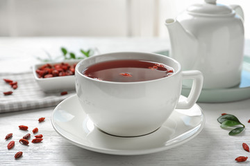 Healthy goji tea in cup on white wooden table