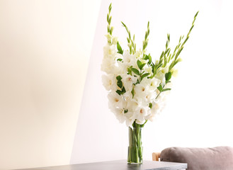 Vase with beautiful white gladiolus flowers on wooden table near color wall. Space for text