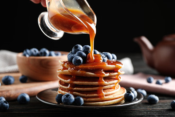 Pouring caramel syrup onto pancakes with fresh blueberries on table