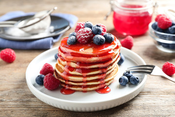 Delicious pancakes with fresh berries and syrup on wooden table