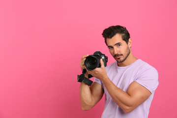 Young photographer with professional camera on pink background. Space for text