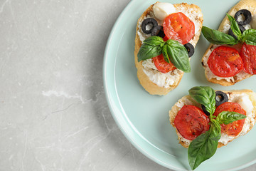 Plate of delicious tomato bruschettas on light grey marble background, top view. Space for text
