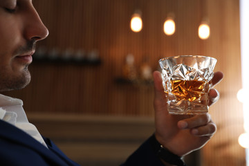 Young man with glass of whiskey indoors, closeup
