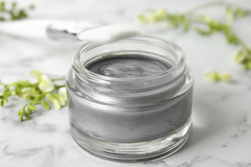 Professional face mask with brush and flowers on white marble table, closeup