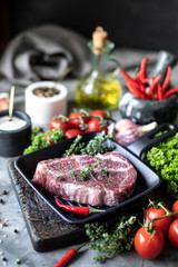 Raw fresh meat. Steak for two with ingredients in a grill pan, with spices, vegetables and herbs
