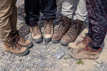Company four tourists only legs together in brown trekking hiking boots with laces on rocky cliff....