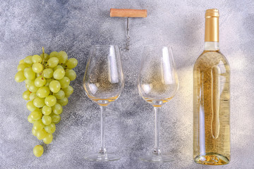 Unopened vintage bottle of white wine without label and bunches of ripe organic grapes on grunged stone table background. Expensive bottle of chardonnay concept. Copy space, top view, flat lay.