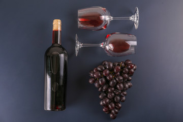 Vintage bottle of red wine without label, corkscrew & bunches of ripe organic grapes on matte blue...
