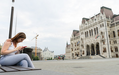 Young red head girl sitting in a bench at the parliament square at Budapest, Hungary. Teenager...