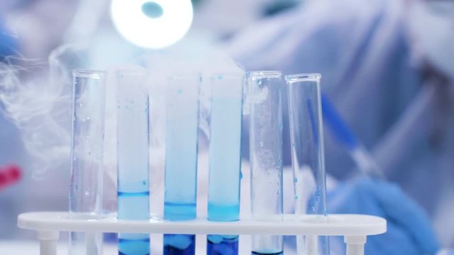 Close up of scientist adding solution with pipette on smoking blue fluid in test tubes. Chemist in research lab.