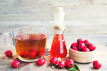 Hawthorn tincture (thornapple, May-tree, whitethorn, hawberry) in glass small bottles and tea in a glass mug on the wooden table. Herbal medicine.