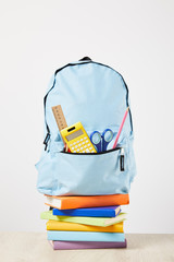 Blue backpack with supplies in pocket on books isolated on white