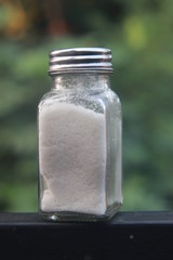 salt from small shaker at garden, green background