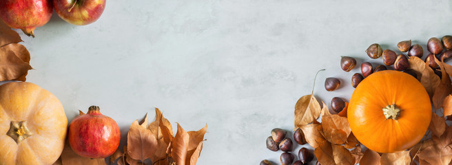 Orange and peachy pumpkins ripe organic red glossy apples pomegranates chestnuts dry yellow autumn leaves on gray marble stone background. Thanksgiving fall harvest abundance. Long banner copy space