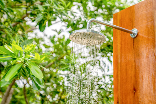 Outdoor shower head stick on the wooden plate pole design for showering body before jumping in the resort pool.