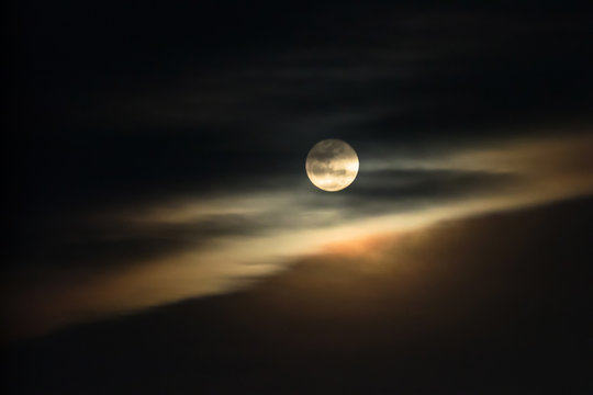 Super moon shining glowing light through the darkness of cloudy night sky; blur image for background